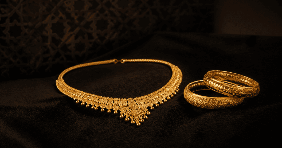 An ornate gold necklace and engraved gold bangles on dark velvet